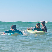 The surf instructor is with the children in the shallow water.